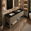 A modern double-sink bathroom vanity with a black countertop, ribbed beige cabinet fronts, and gold hardware, shown in a luxurious bathroom setting with warm lighting and marble flooring.