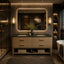 A luxury modern bathroom vanity featuring a double sink with a dark green marble countertop, a light wood cabinet with brass handles, a large backlit mirror, and warm wall sconces.