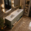 A modern double-sink bathroom vanity with a white countertop, matte green textured cabinet doors, and gold hardware, set in a luxurious bathroom with warm lighting and marble flooring.