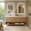 A modern double-sink bathroom vanity with a light wood slat front, white countertop, and two backlit rectangular mirrors. The vanity is shown in a bright, contemporary bathroom with a glass shower enclosure, window view, and folded white towels on the open shelf.