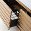 A close-up of a light natural wood vanity or cabinet drawer pulled open, showing a black organizer tray with white compartments holding two amber bottles.