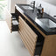 A modern floating bathroom vanity with a black stone countertop, integrated sinks, and light wood slat-front drawers with one open drawer showing storage bins.