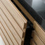 Close-up of a light oak wood kitchen cabinet drawer with a slatted front and dovetail joint, shown next to a black countertop.