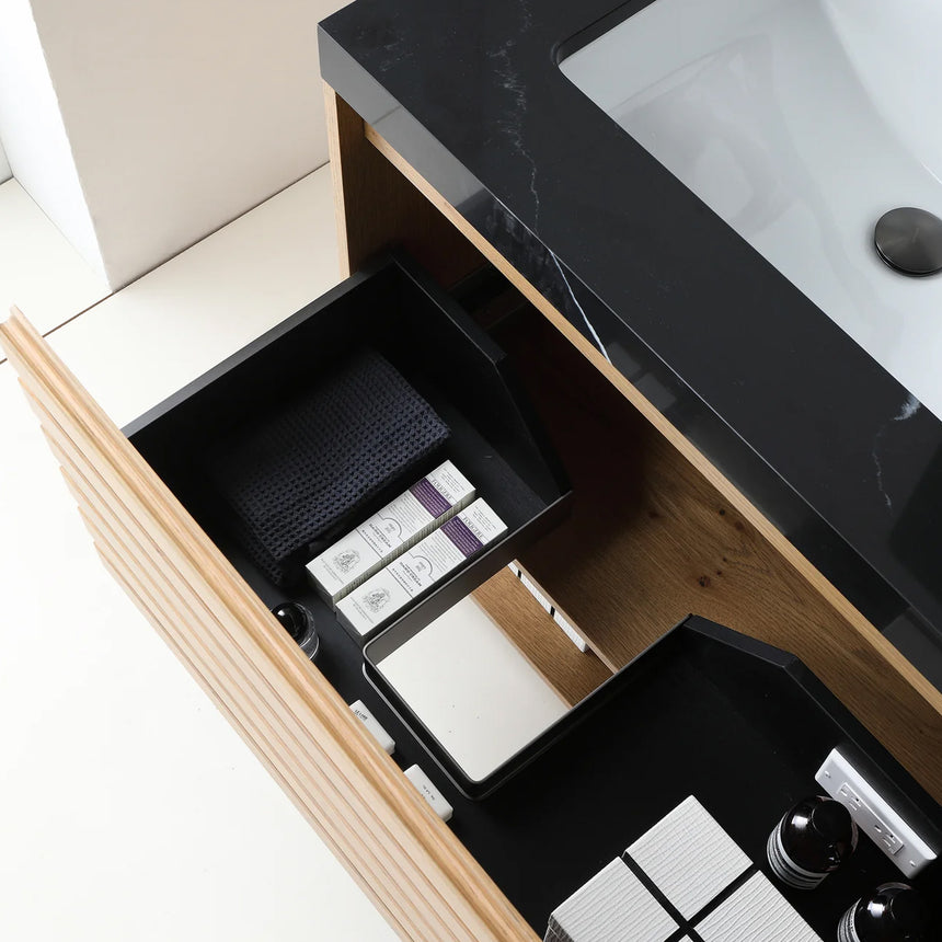 A modern floating bathroom vanity with a light oak wood finish, a white countertop, and an integrated sink, shown in a styled bathroom setting with a bathtub, shower glass, and decorative plants.