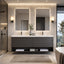 A modern double-sink bathroom vanity in a sleek gray wood finish, set against a light beige tiled wall with illuminated rectangular mirrors. The vanity features a white countertop with integrated sinks, open shelving below for towels and accessories, and is styled with a small vase of greenery.