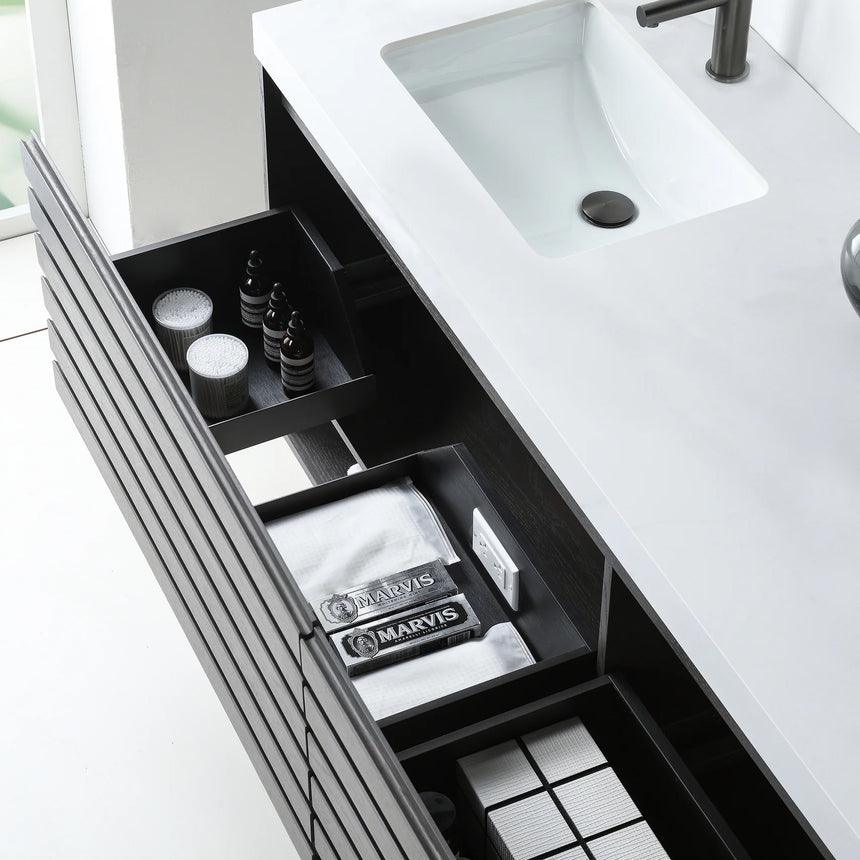 A modern floating bathroom vanity with a light oak wood finish, a white countertop, and an integrated sink, shown in a styled bathroom setting with a bathtub, shower glass, and decorative plants.