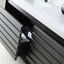 Close-up of a modern bathroom vanity with dark charcoal gray slatted drawers, a white countertop, and an open drawer showing a black storage pocket holding a Mary's toothbrush holder.