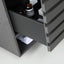 Close-up of a dark gray wooden drawer with a pull handle, partially open to reveal a shelf inside containing toiletry bottles and a folded white towel.