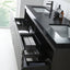 A modern black bathroom vanity with integrated sinks, a matte black faucet, and multiple open drawers showing storage compartments and folded towels. Decorative bottles and a vase sit on the countertop in a bright, minimalist bathroom setting.