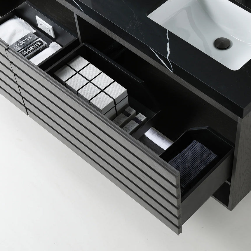 A modern floating bathroom vanity with a light oak wood finish, a white countertop, and an integrated sink, shown in a styled bathroom setting with a bathtub, shower glass, and decorative plants.