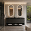 A modern double-sink bathroom vanity with two illuminated oval mirrors, a dark floating console, and a spa-like bathroom setting with a glass shower and bathtub visible.