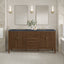 Bathroom vanity with two mirrors, lights, and decorative items against a neutral wall.