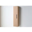A tall, narrow wall-mounted cabinet in a light natural wood finish with a slim black vertical handle, shown against a plain light gray wall.