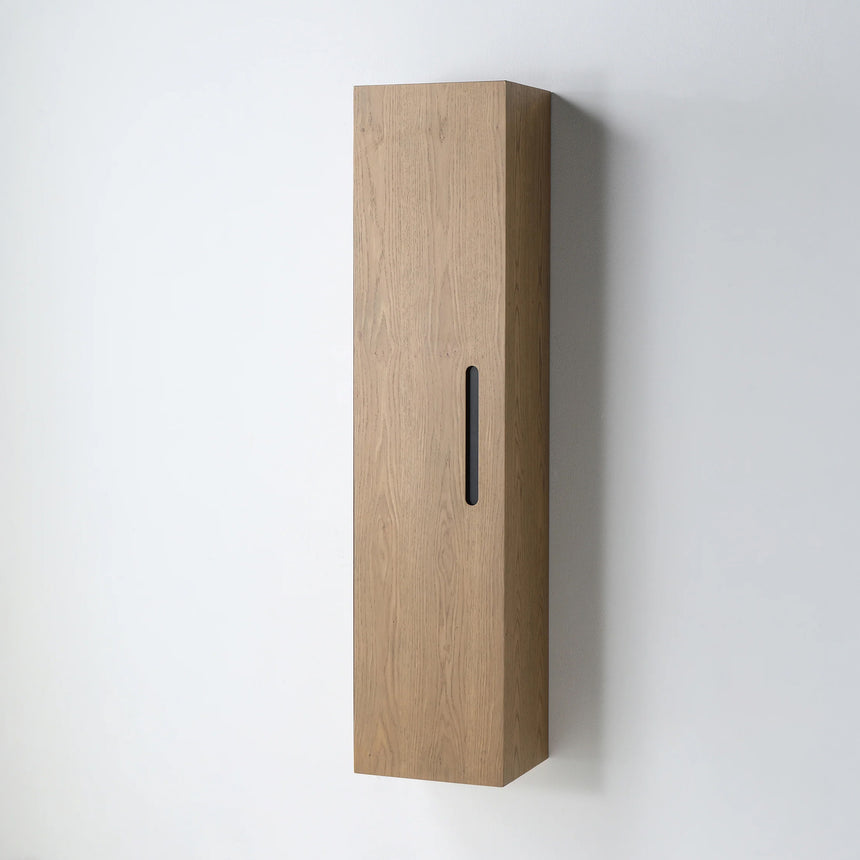 A tall, narrow wall-mounted cabinet in a light natural wood finish with a slim black vertical handle, shown against a plain light gray wall.