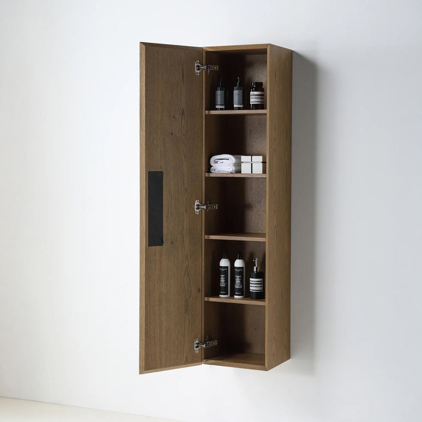 A tall, narrow wall-mounted cabinet in a light natural wood finish with a slim black vertical handle, shown against a plain light gray wall.