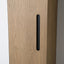 A close-up of a light oak wood cabinet door featuring a minimalist, vertically oriented matte black metal pull handle.