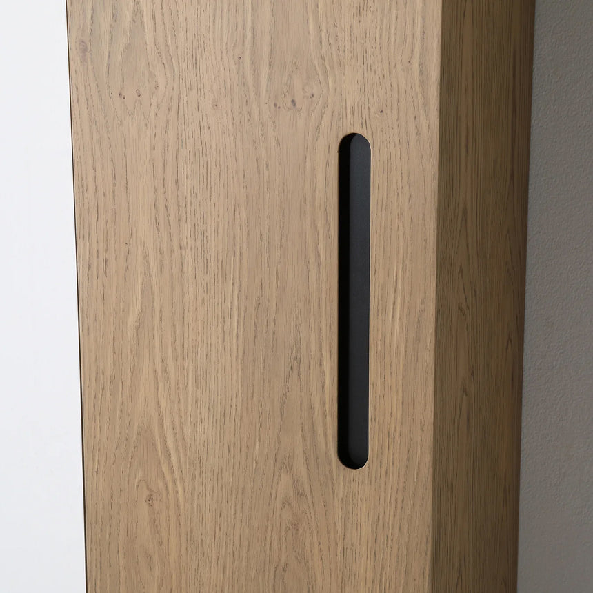A tall, narrow wall-mounted cabinet in a light natural wood finish with a slim black vertical handle, shown against a plain light gray wall.