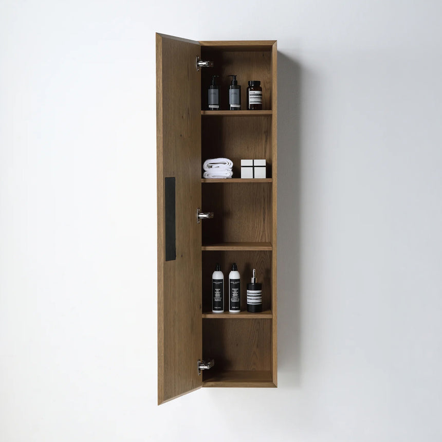 A tall, narrow wall-mounted cabinet in a light natural wood finish with a slim black vertical handle, shown against a plain light gray wall.