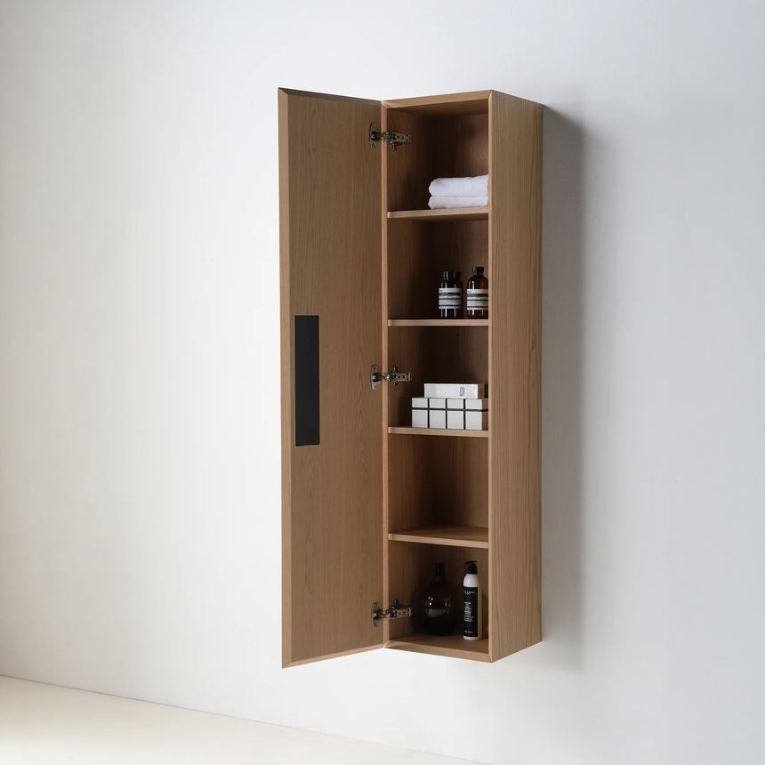 A tall, narrow wall-mounted cabinet in a light natural wood finish with a slim black vertical handle, shown against a plain light gray wall.
