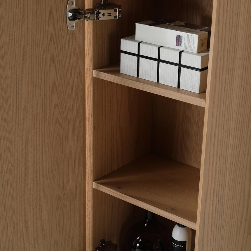 A tall, narrow wall-mounted cabinet in a light natural wood finish with a slim black vertical handle, shown against a plain light gray wall.