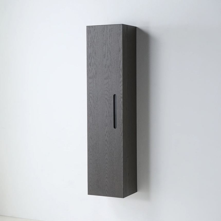 A tall, narrow wall-mounted cabinet in a light natural wood finish with a slim black vertical handle, shown against a plain light gray wall.