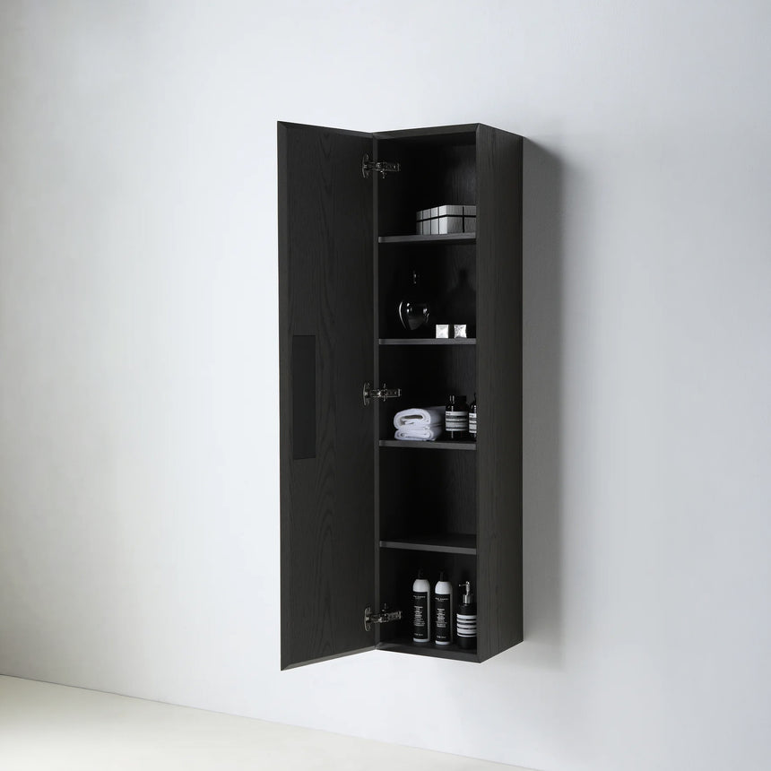 A tall, narrow wall-mounted cabinet in a light natural wood finish with a slim black vertical handle, shown against a plain light gray wall.