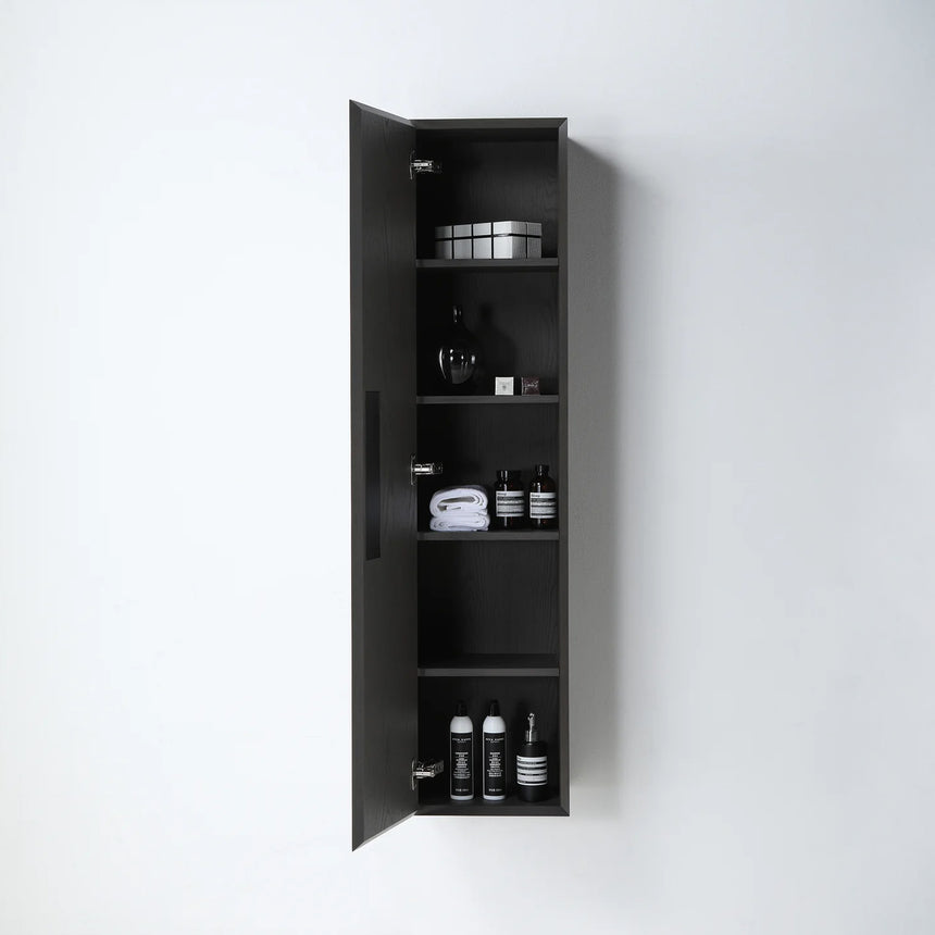 A tall, narrow wall-mounted cabinet in a light natural wood finish with a slim black vertical handle, shown against a plain light gray wall.