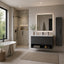 Modern floating bathroom vanity in a minimalist beige-toned bathroom, featuring a dark gray wood-look cabinet with an integrated white sink, a large backlit rectangular mirror, and a tall matching storage cabinet beside it.