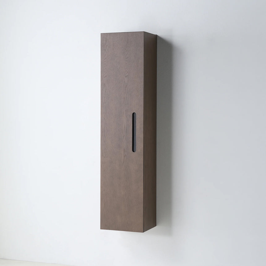 A tall, narrow wall-mounted cabinet in a light natural wood finish with a slim black vertical handle, shown against a plain light gray wall.
