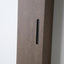 Close-up of a dark brown wood cabinet door with a slim black vertical handle, set against a light gray wall.