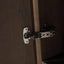 Close-up of a modern hinge mounted on a dark brown wooden cabinet door next to a vertical wood trim strip.
