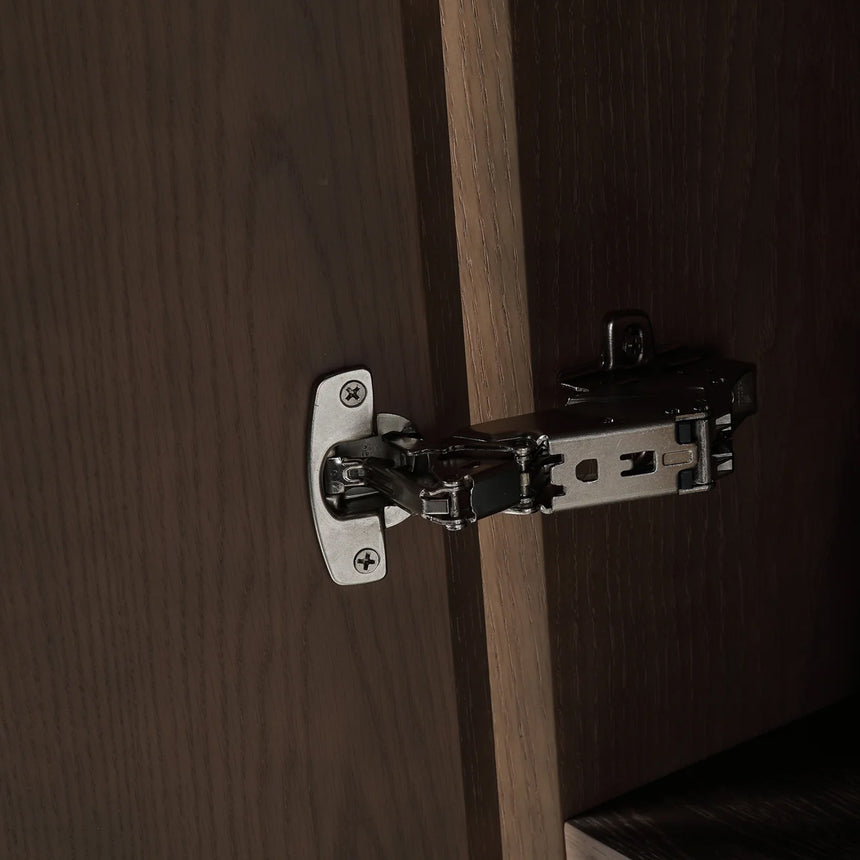 A tall, narrow wall-mounted cabinet in a light natural wood finish with a slim black vertical handle, shown against a plain light gray wall.