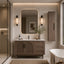 A modern bathroom vanity setup in a warm neutral interior, featuring a brown wooden cabinet with cane-style doors, a white marble countertop, a large rounded rectangular mirror with a warm light border, matching wall sconces, a tall storage cabinet, and a freestanding bathtub partially visible on the right.