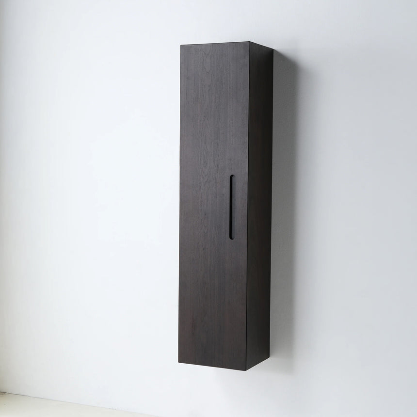 A tall, narrow wall-mounted cabinet in a light natural wood finish with a slim black vertical handle, shown against a plain light gray wall.