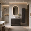A modern bathroom interior featuring a dark wood vanity with a white sink, an illuminated oval mirror, a tall matching cabinet, and a walk-in shower area in the background.