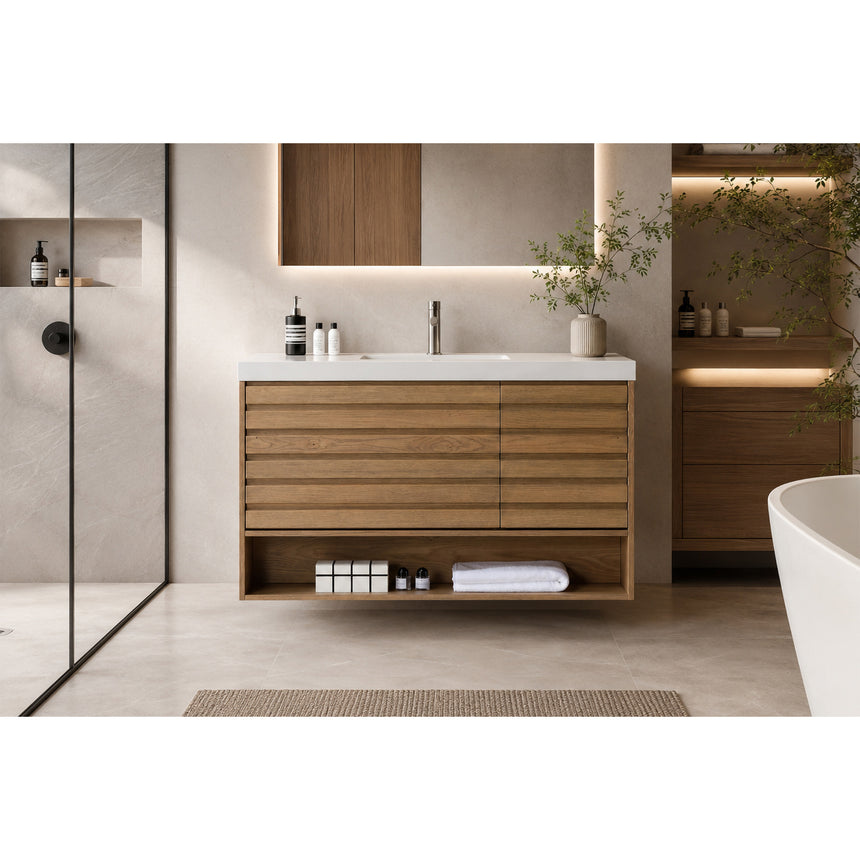 A modern floating bathroom vanity with a light oak wood finish, a white countertop, and an integrated sink, shown in a styled bathroom setting with a bathtub, shower glass, and decorative plants.