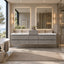 A modern floating double-sink bathroom vanity in a light gray stone finish, set in a bright, contemporary bathroom with illuminated mirrors, a bathtub, and a glass shower enclosure.