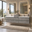 A modern floating double-sink bathroom vanity in a light gray stone or concrete finish with white countertops, set in a bright contemporary bathroom with illuminated mirrors, wall sconces, and a large window view.
