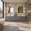A modern double-sink bathroom vanity in a minimalist bathroom setting, featuring a floating gray concrete double vanity with integrated white basins, two backlit rectangular mirrors, and wall-mounted light bars. A freestanding white bathtub is partially visible on the left, and a glass-enclosed shower is on the right.