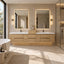 A modern bathroom interior featuring a double vanity with two illuminated rectangular mirrors, light wood floating cabinets, white sinks, and a freestanding bathtub in a bright, sunlit room.