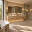 A modern bathroom interior with a floating double-sink vanity in light wood, white countertops, a large illuminated mirror, wall sconces, a glass shower enclosure, and a freestanding white bathtub in the foreground.